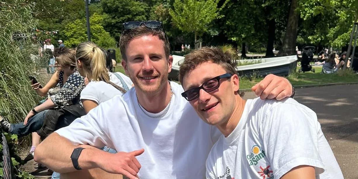 Greg sitting in a park with a friend, both smiling at the camera