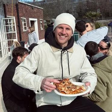 Greg holding a plate of pizza, surrounded by friends outdoors