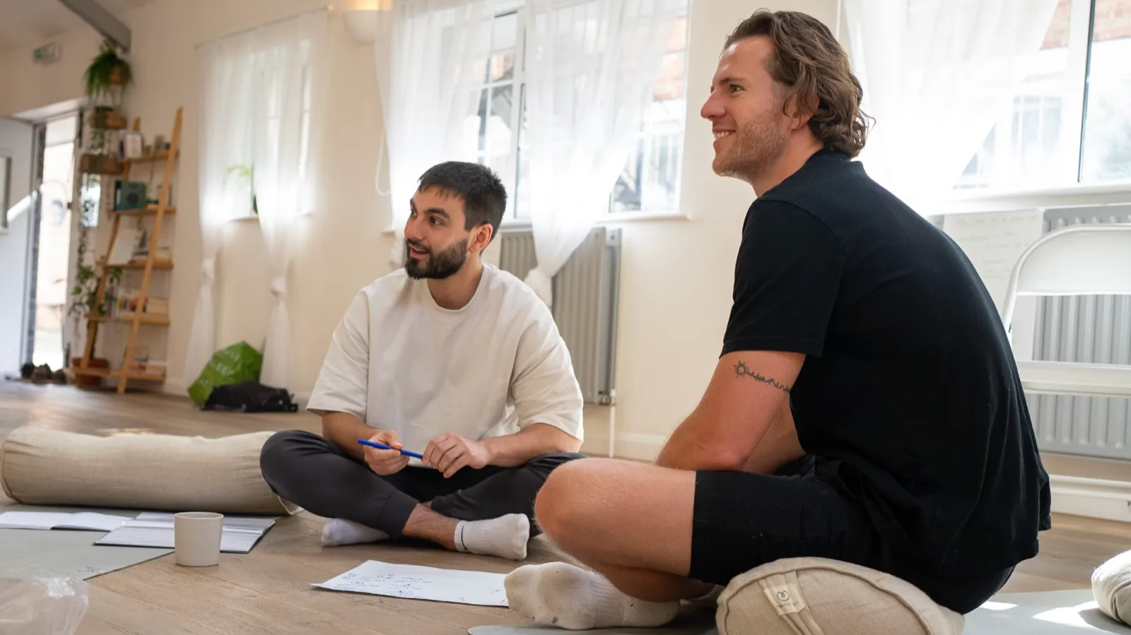 Two men sitting on the floor of a bright studio during Men's Circle facilitator training