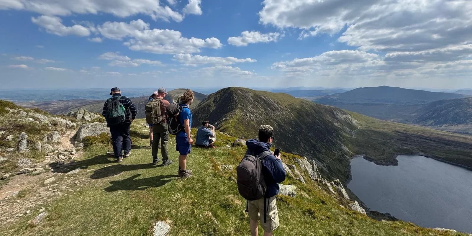 A Men's Circle group on a mountain ridge above a lake, looking out across the valley