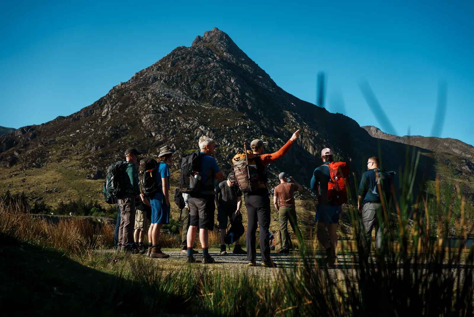 A group of men with backpacks on a Men's Circle retreat, gathered below a mountain peak