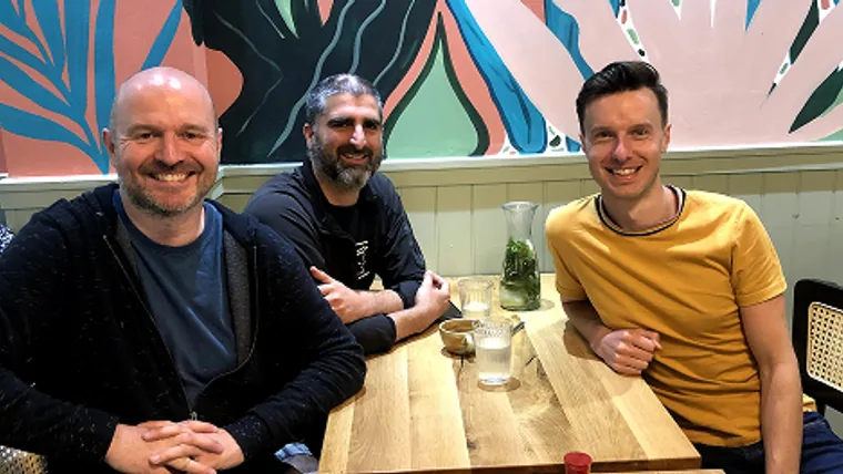 Three of the original men sitting around a café table in London