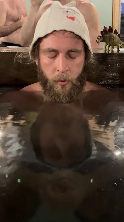 A man in a sauna hat resting at the surface of a cold plunge